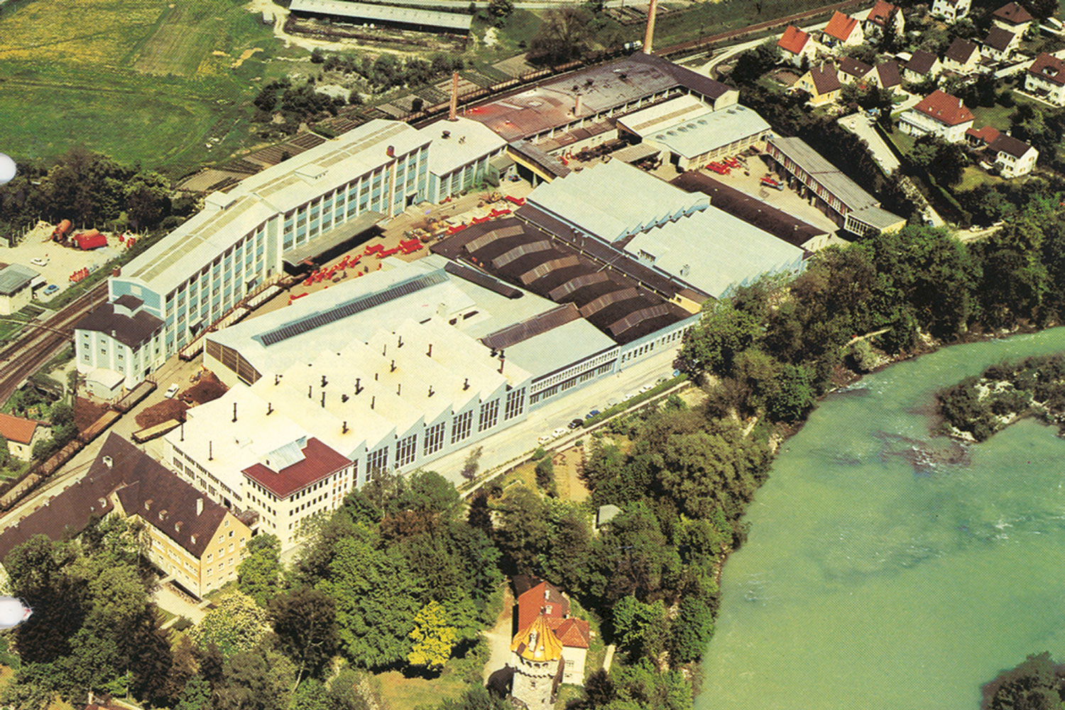 Majestátní Bayerische Pflugfabrik v Landsbergu mezi železniční tratí a řekou Lech.